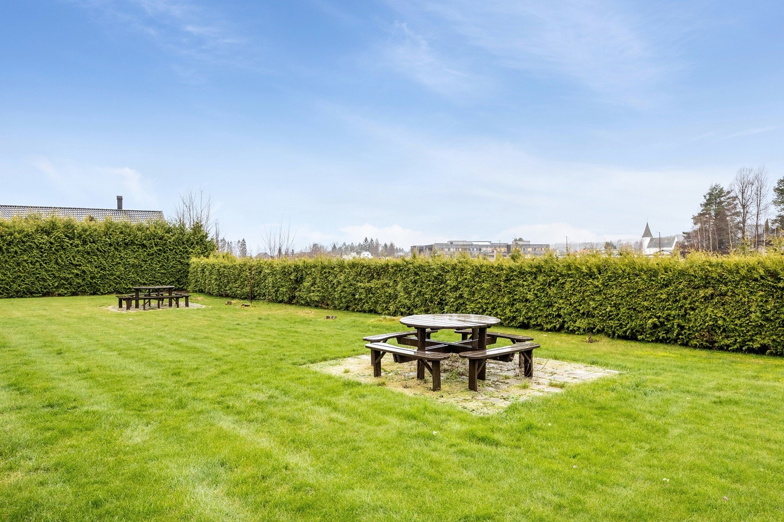 I en velstelt og solrik hage er det satt ut sittebenker til felles anvendelse. Galleribilde