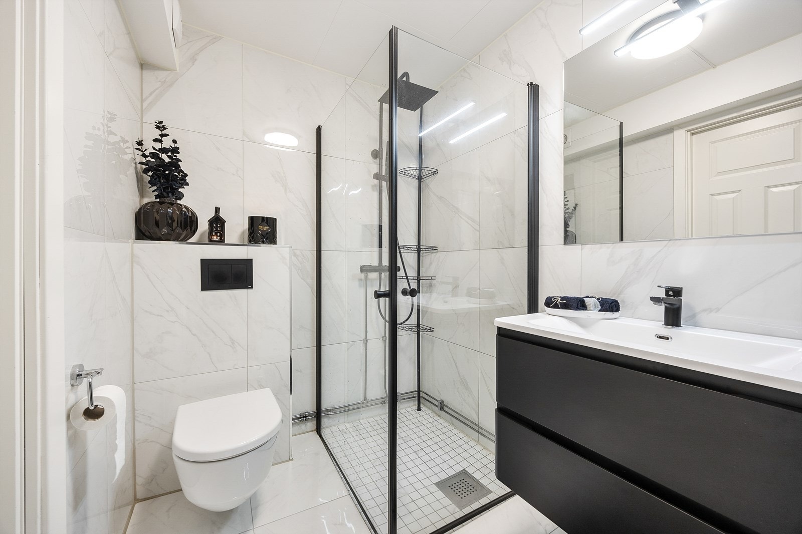 Badet er utstyrt med dusjhjørne med innfellbare glassvegger, vegghengt wc og servantinnredning med skuffer Galleribilde