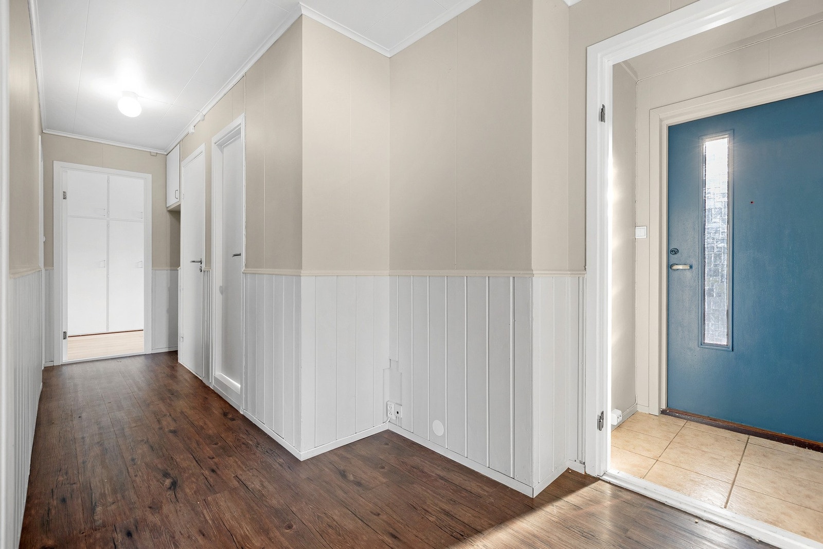 Lyst gangområde med brystningspanel på vegger og laminatgulv. Enkel entre med flislagt gulv. Galleribilde