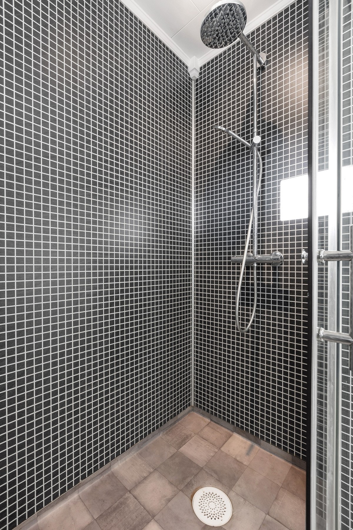 Dusj med sorte mosaikkfliser på veggene og grå fliser på gulvet. Galleribilde