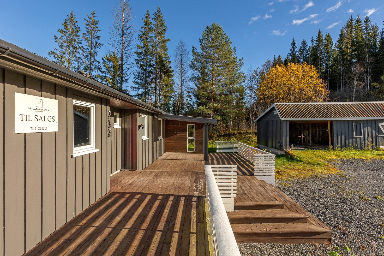 Utendørsområde med treplatting, gruslagt innkjørsel og garasje. Solrik beliggenhet med skog i bakgrunnen. Galleribilde