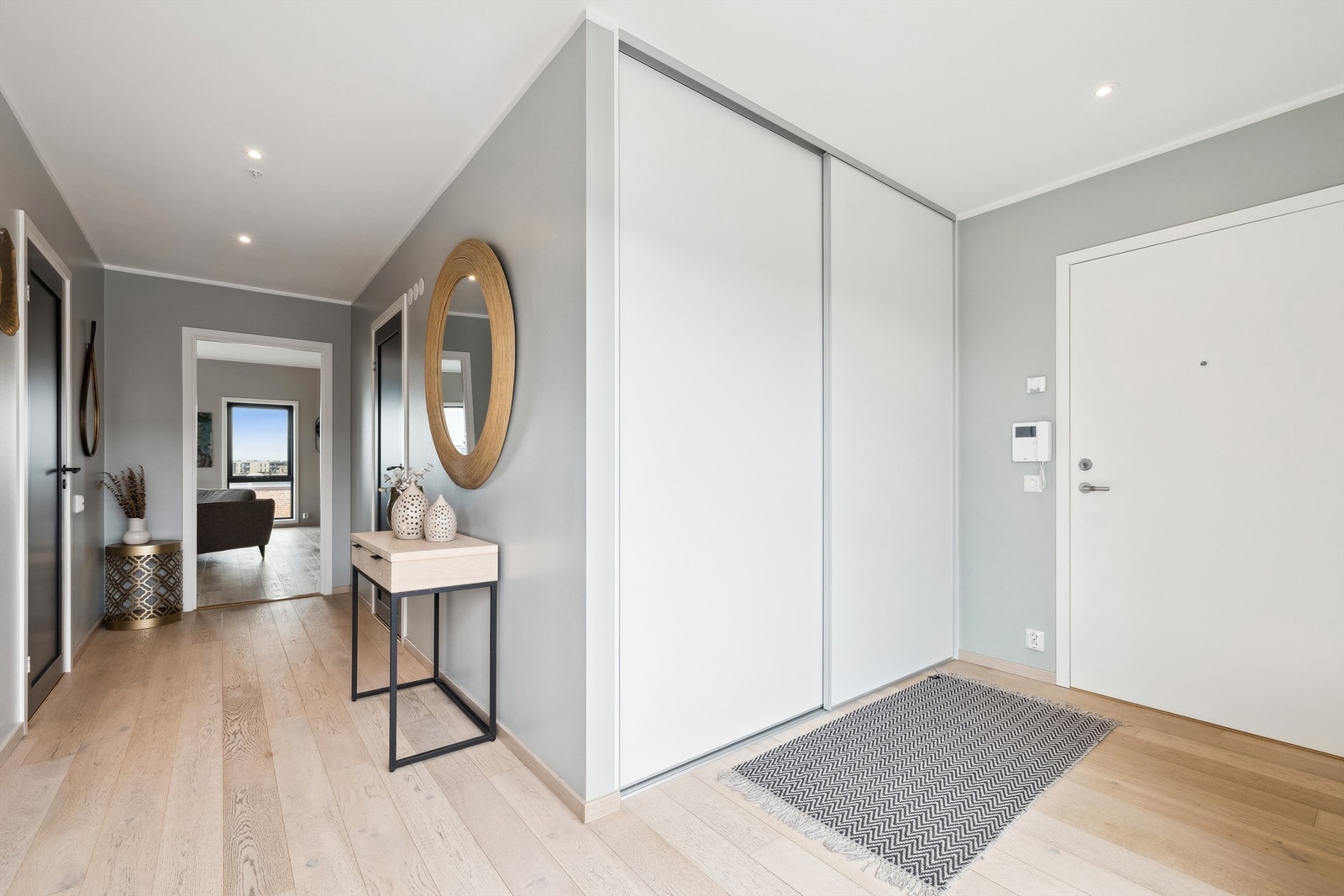 Entreen har gjennomført stil med lys enstavs parkett, grå, slette vegger og innfelte downlights samt bred, plassbygd skyvedørsgarderobe Galleribilde