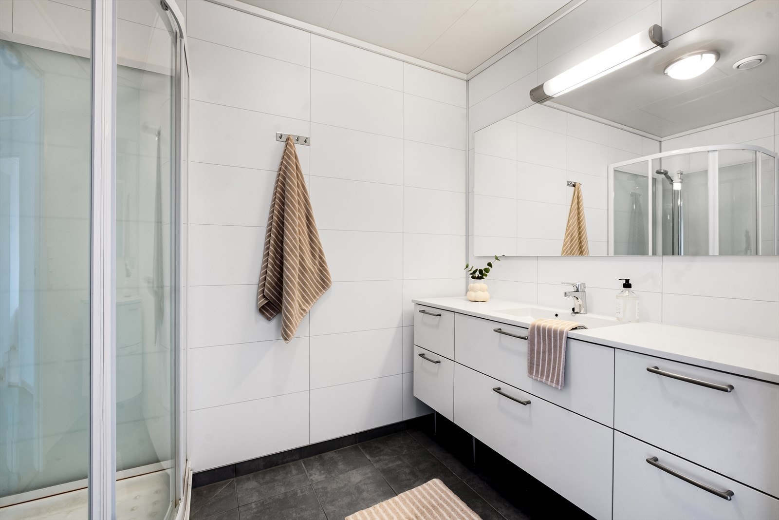 Rommet er utstyrt med innredning med nedfelt servant, veggmontert toalett og dusjkabinett. Galleribilde