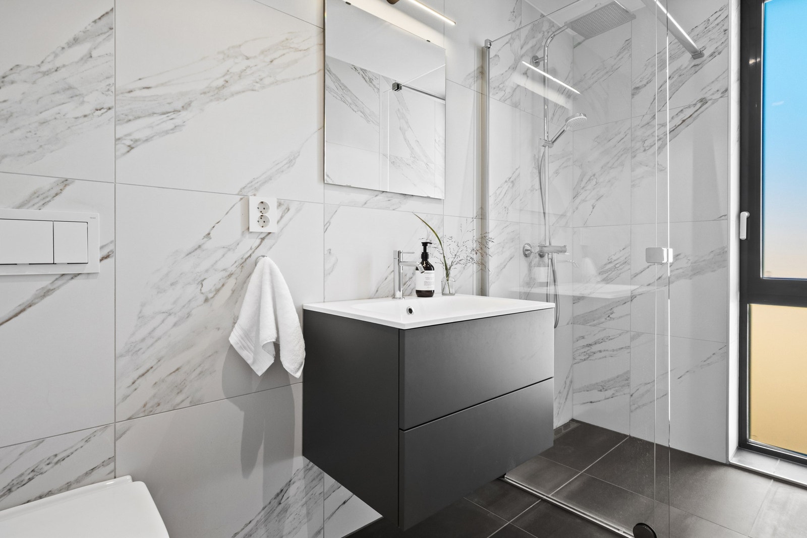 Badet har flislagte gulv og vegger, innredet med servant, vegghengt toalett og dusjhjørne. Galleribilde