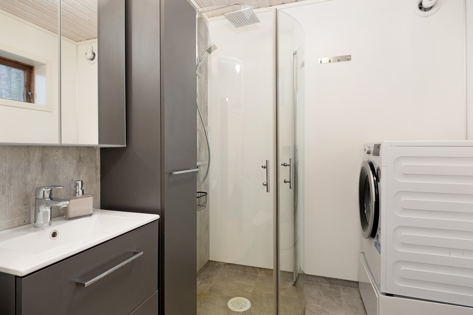 Badet er innreia med dusjhjørne, nedfeltservant med underskuffer, sideskåp, spegel med skåpplass, opplegg for vaskemaskin og toalett. Galleribilde