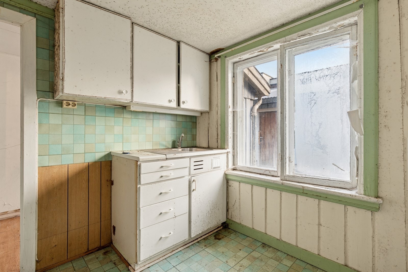 Kjøkkenet har eldre innredning med slette, malte fronter og benkebeslag i stål. Ingen ventilasjon. Galleribilde