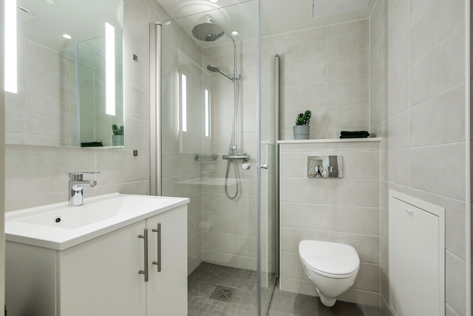 Bad 2 er et stilig bad med pen baderomsinnredning, dusjhjørne med glassvegg, vegg hengt toalett og fliser på gulv Galleribilde