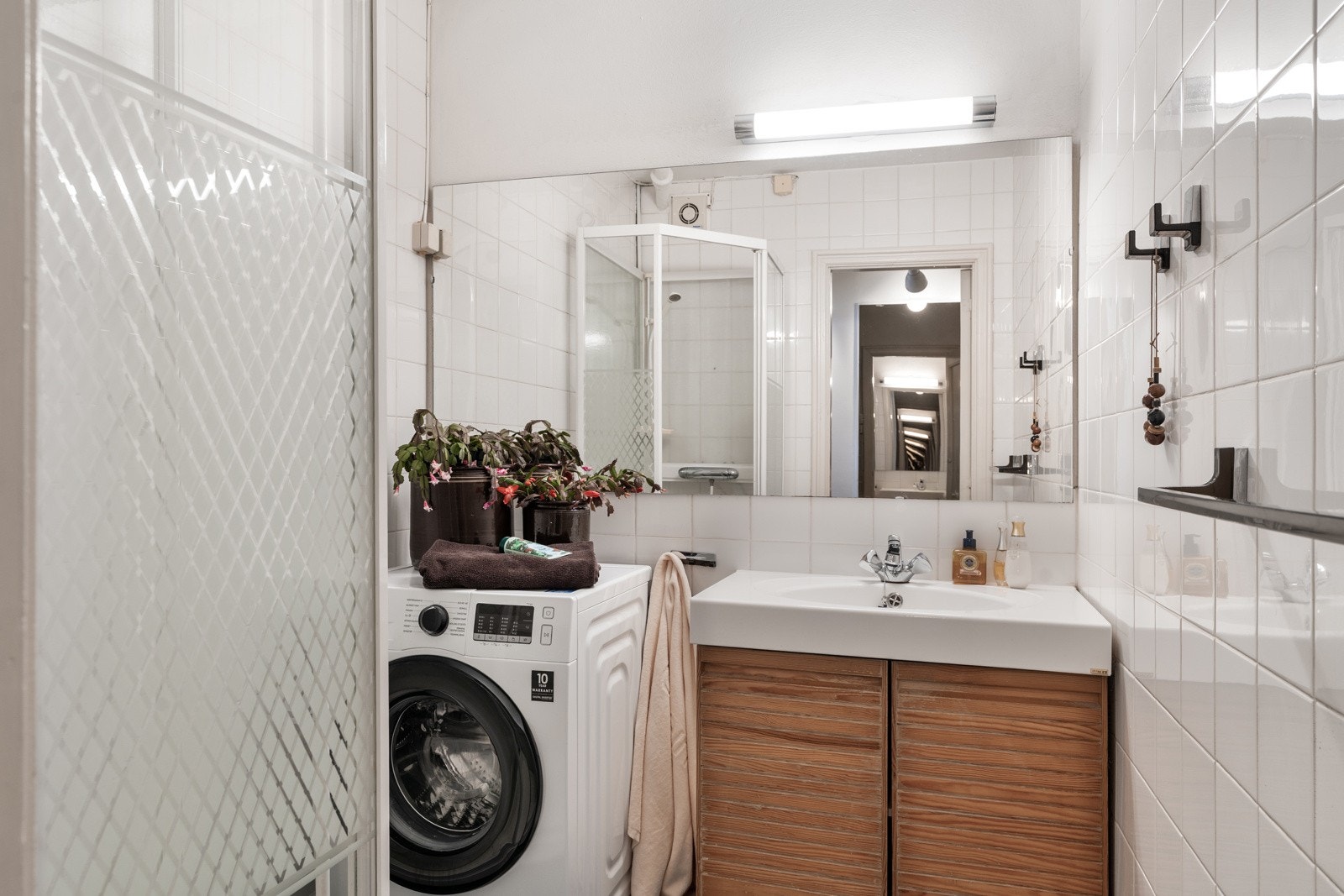 Lyst og funksjonellt flislagt bad med dusj, servant med underbygg og opplegg for vaskemaskin. Galleribilde