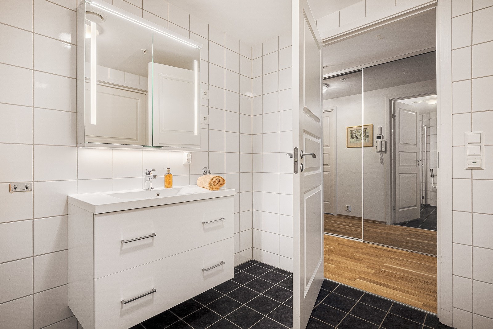 Badet inneholder vegghengt toalett, benkeskap med servant, og dusjdører i glass. Galleribilde