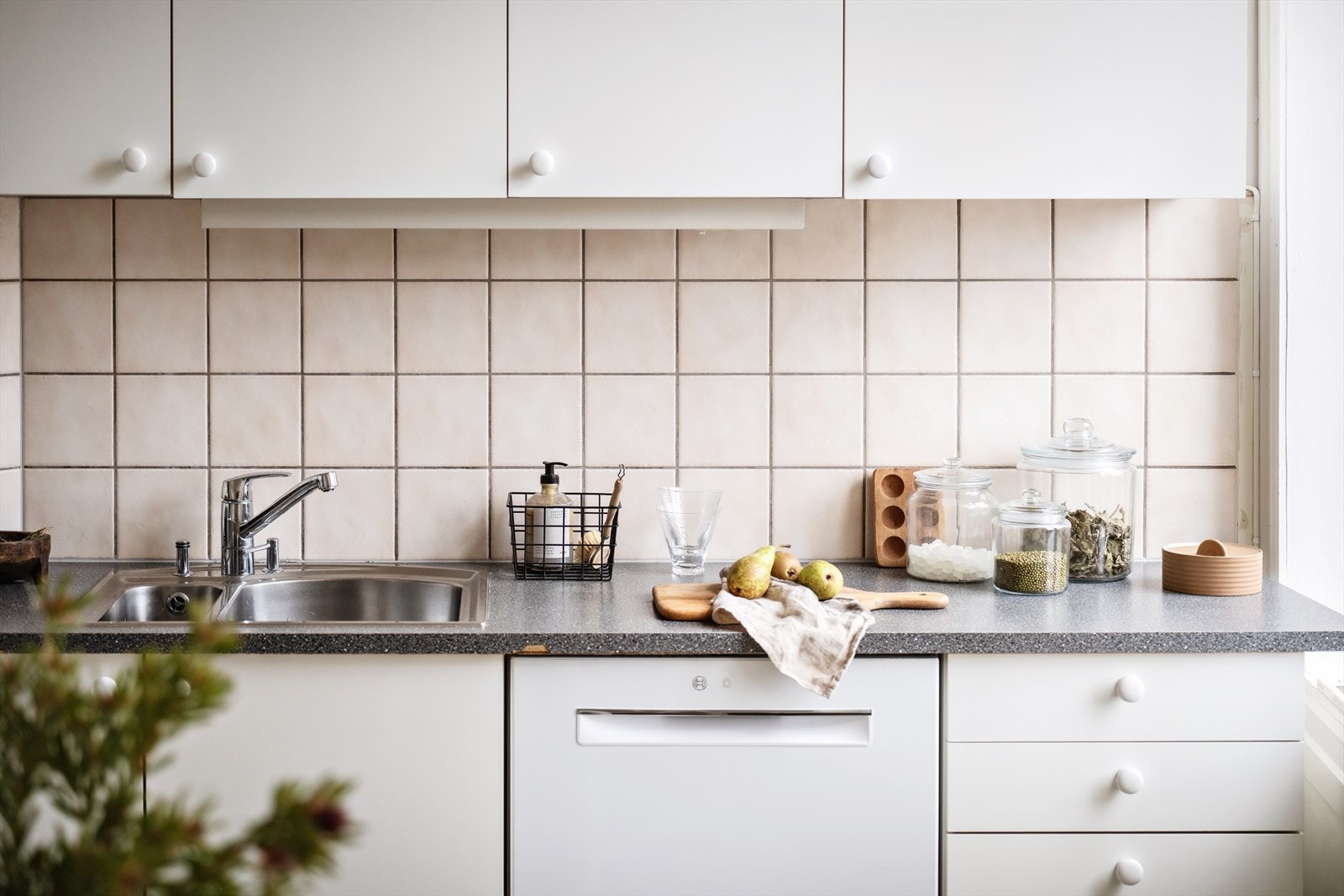 Enkel innredning med slette fronter, fliser og belysning over laminat benkeplate med oppvaskkum og blandebatteri. Galleribilde