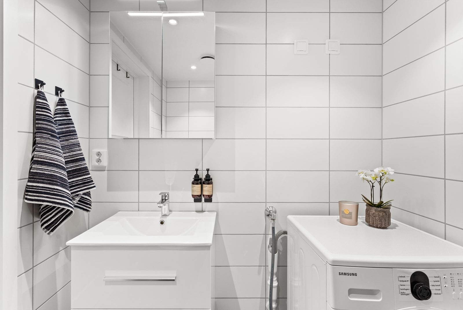 Innredet med servant med underskap, speilskap med belysning, vegghengt toalett, dusjdører og opplegg til vaskemaskin. Galleribilde