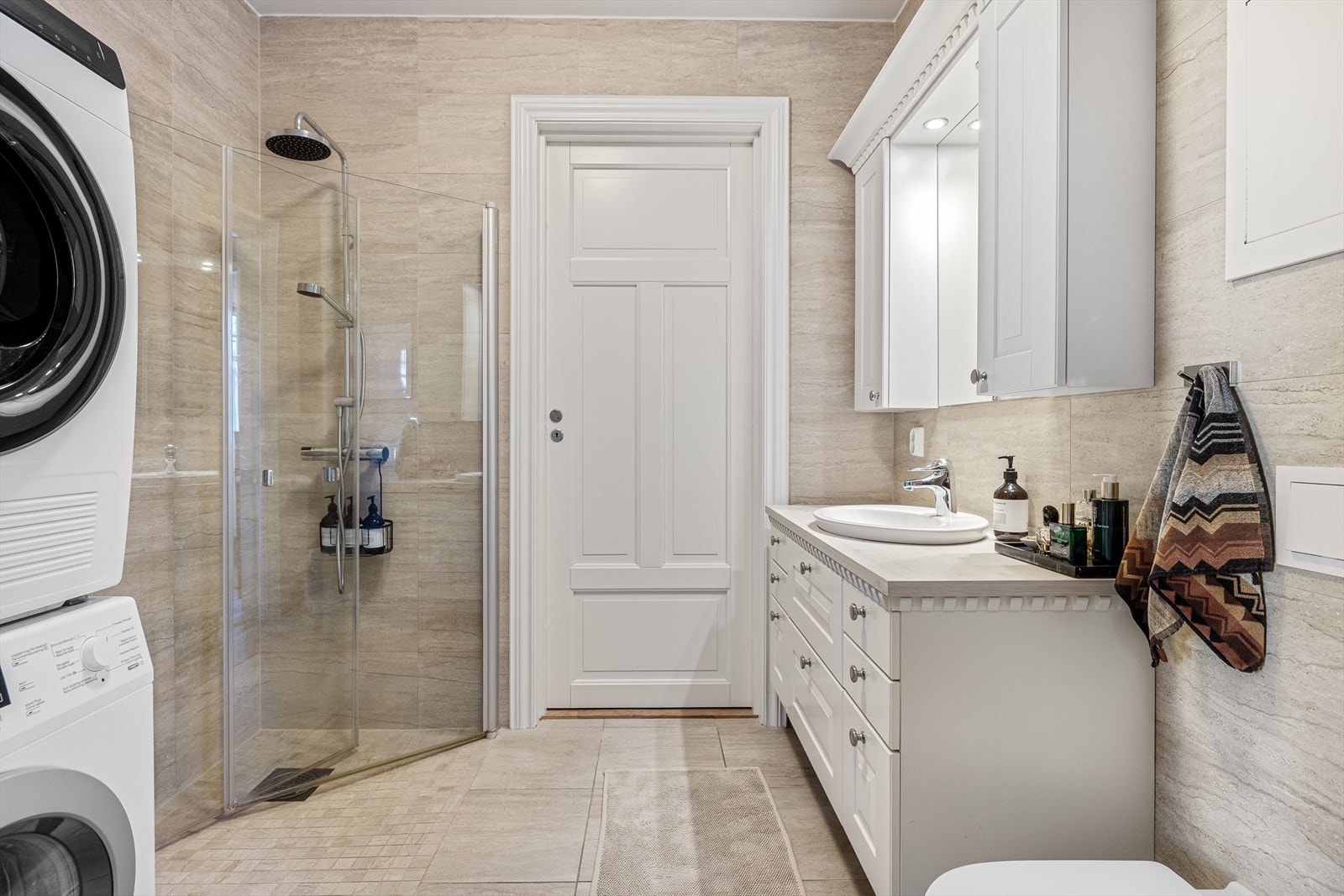 Det er godt med innredning, inkludert servantskap, speil, to veggskap og et praktisk dusjhjørne med glassdører. Det vegghengte klosettet gjør renhold enklere og gir et moderne preg. I tillegg finnes det opplegg til vaskemaskin. Galleribilde