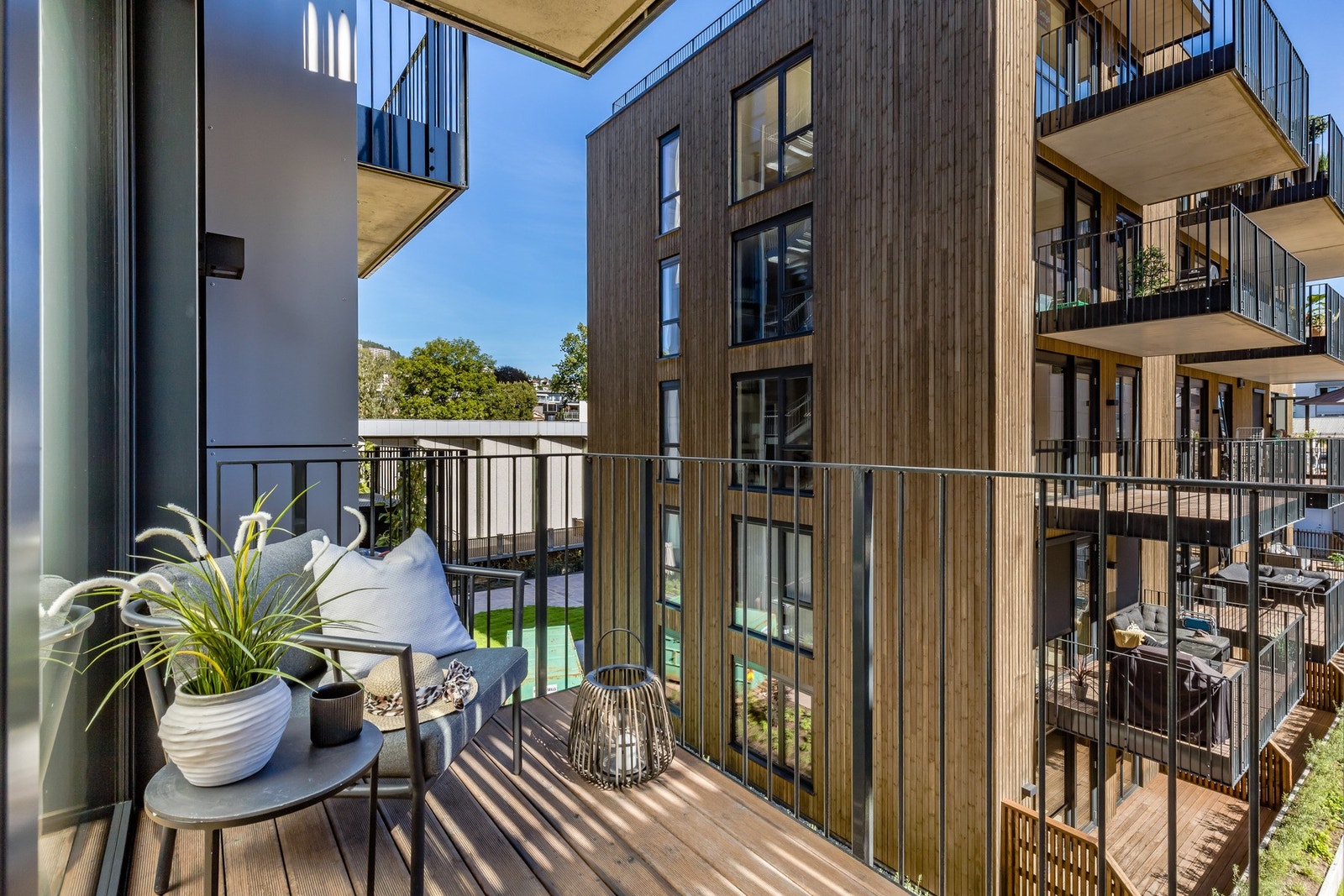 Denne balkongen er også overbygd og har brunbeiset gulv, sprinklet, sort rekkverk og en spilevegg. Galleribilde