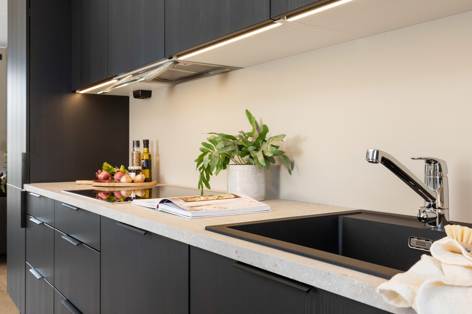 Innredningen har glatte, sorte fronter, benkeplate i lys kompaktlaminat og sort vaskekum. Led-lyslister sikrer godt med belysning til matlagingen. Galleribilde