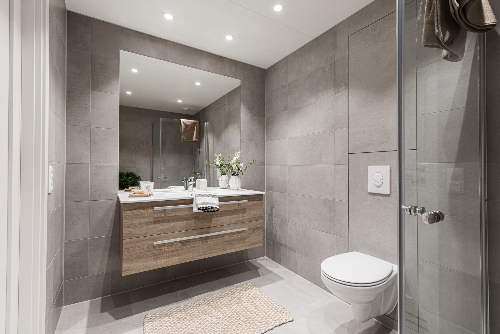 Badet har lekre, ulike fliser i grått med en anelse lysere nyanse på gulvet. Rommet har gulvvarme, downlights og opplegg for vaskerom og tørketrommel. Galleribilde