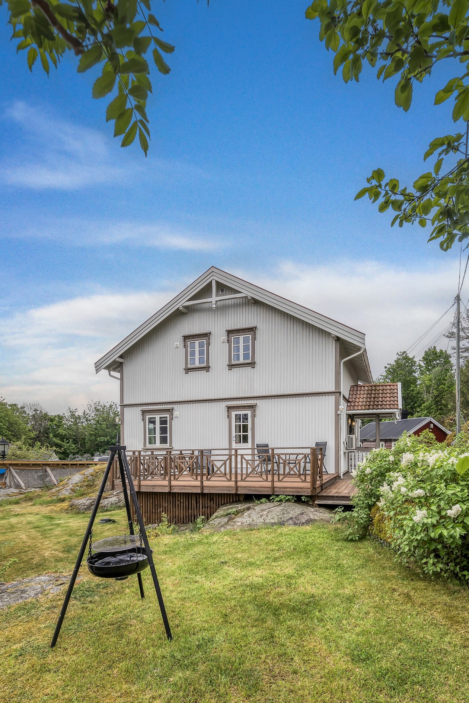 Flott hage med plen, prydbusker og trær innimellom bergknauser i et typisk kystnært landskap. Galleribilde