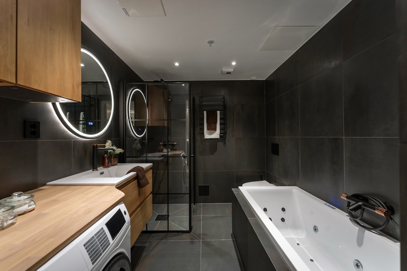 Dette badet ligger tilknyttet hovedsoverommet via garderoberommet. Her er det valgt mørke storformatfliser på gulv og vegger, samt sorte armaturer med kobberdetaljer som gir et elegant og eksklusivt inntrykk. Galleribilde