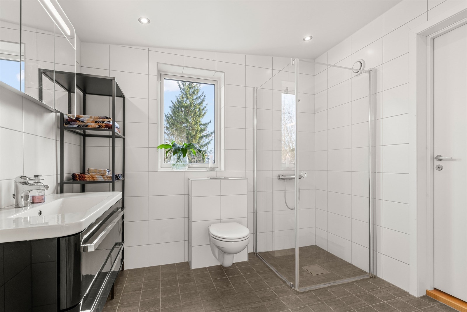 Badet i andre etasje er stilrent, helfliset og har en praktisk dusjnisje med glassdør. Galleribilde