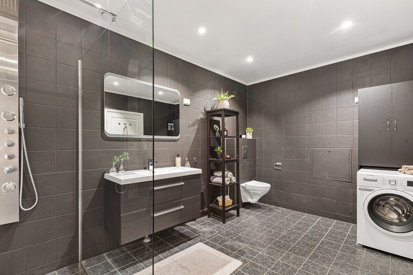 Badet er praktisk innredet med dusjhjørne, veggmontert toalett og opplegg for vaskemaskin. Galleribilde