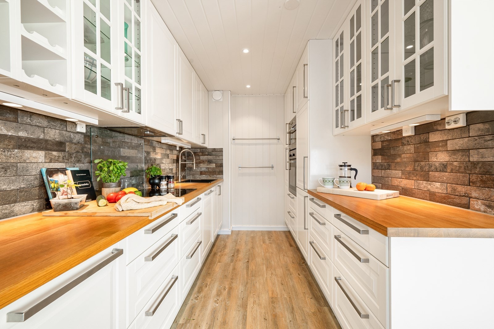 Kjøkkenet er godt opplyst med utstrakt bruk av downlights som skaper en behagelig og funksjonell arbeidsbelysning. Integrerte hvitevarer sørger for et rent og gjennomført helhetsinntrykk - et kjøkken som kombinerer praktiske løsninger med tidløs estetikk. Galleribilde