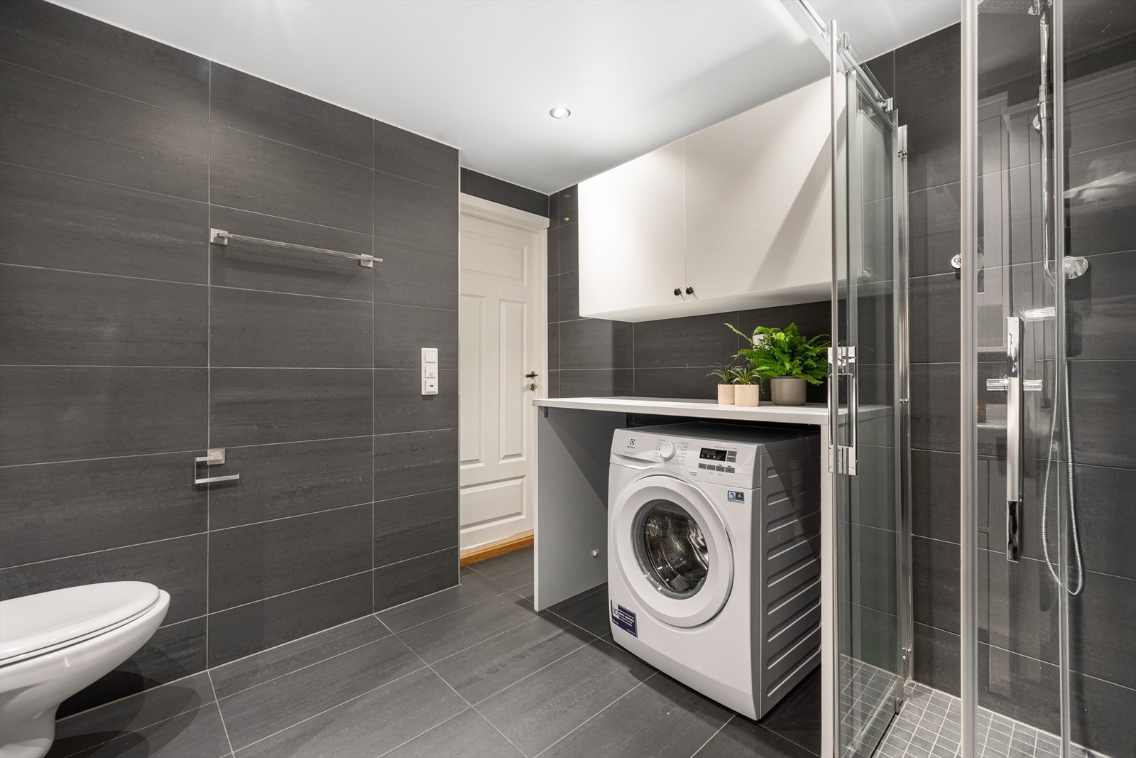 Baderommet er praktisk innredet med plass til både vaskemaskin og tørketrommel hvis ønskelig under benkeplate som gir gode arbeidsflater når klesvasken skal brettes og sorteres. Galleribilde