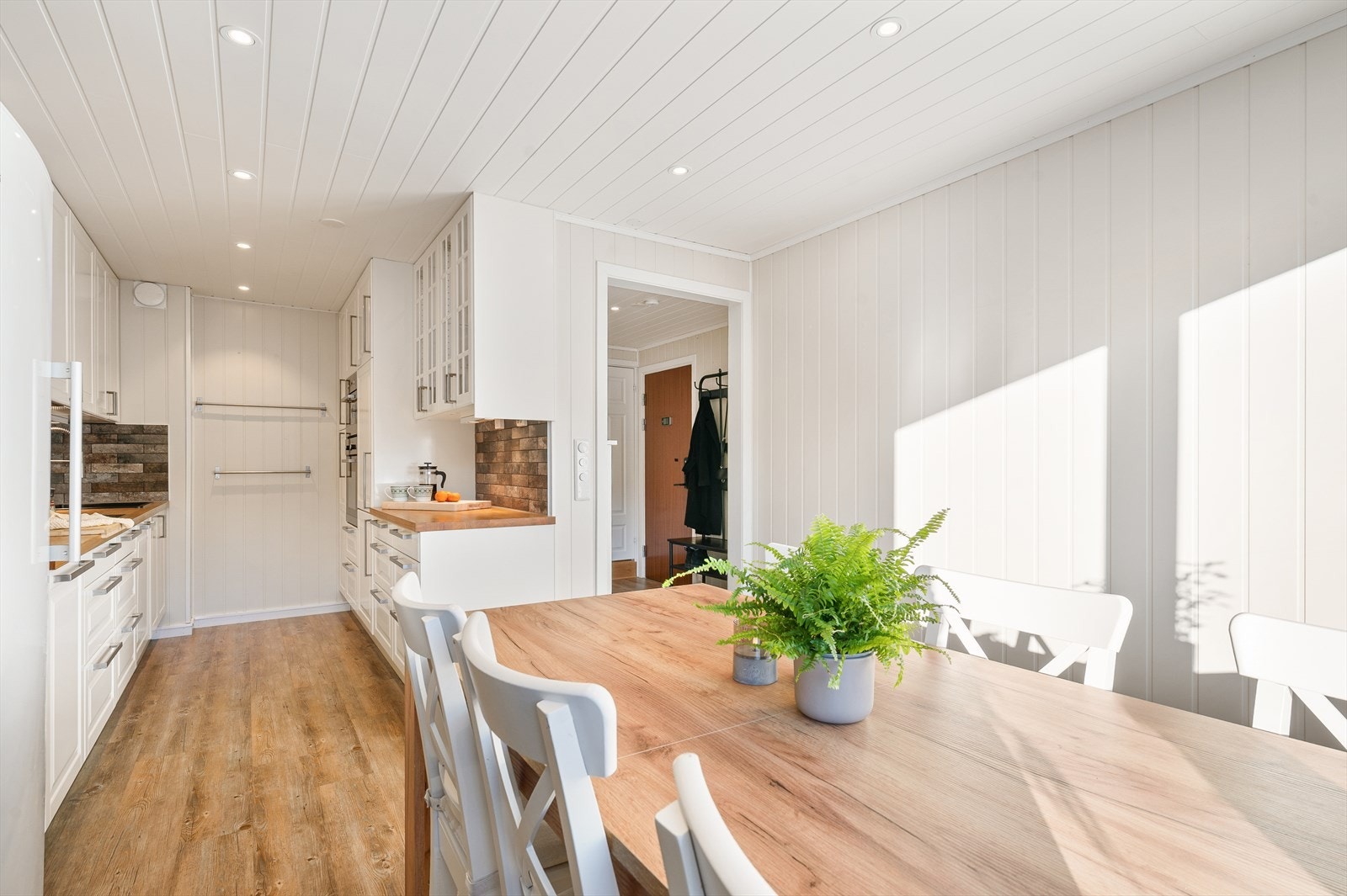 De takhøye skapene sørger for optimal oppbevaring, mens vitrineskapene tilfører både karakter og en luftig følelse. Mellom kjøkkenbenk og overskap finner du dekorative og slitesterke steinfliser som fremhever kjøkkenets kvaliteter. Galleribilde