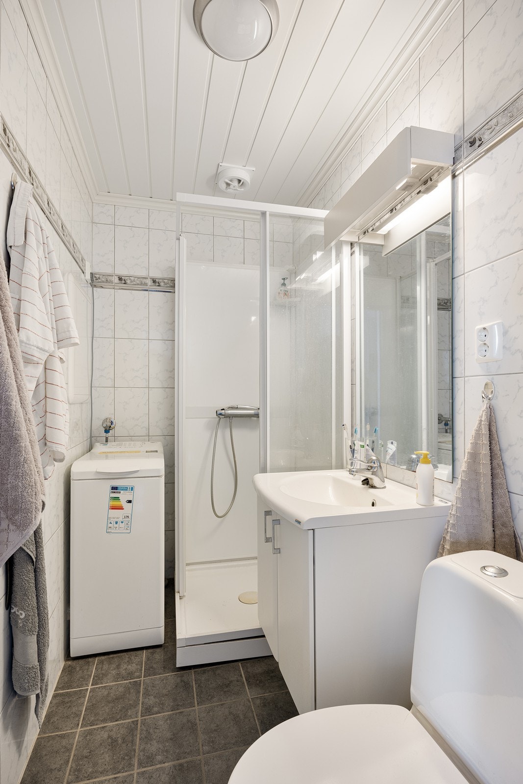 Flislagt bad innredet med dusjkabinett, servant i servantskap, toalett og opplegg for vaskemaskin. Galleribilde