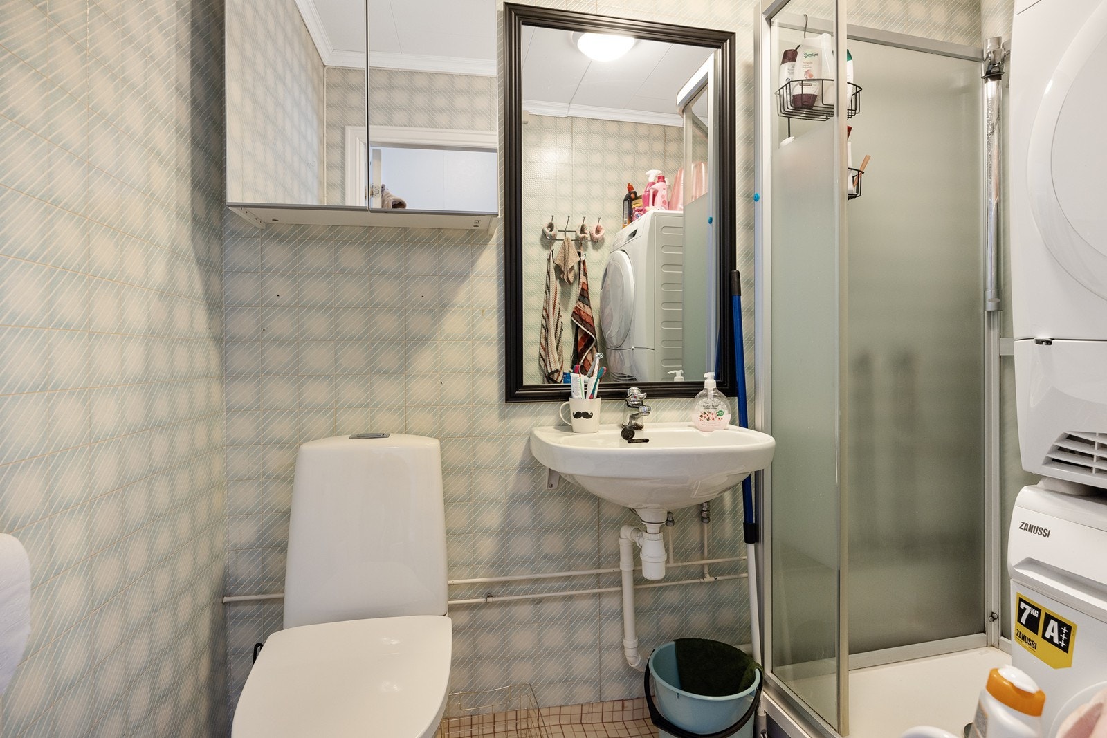 Baderom innredet med toalett, speilskap, dusjkabinett, servant og opplegg for vaskemaskin. Galleribilde