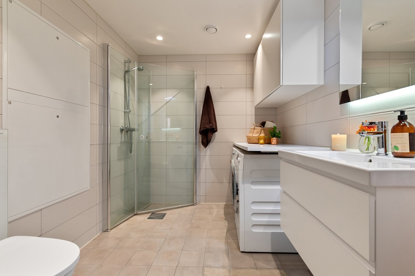 Stort flislagt bad med praktisk innredning for vaskemaskin og tørketrommel Galleribilde