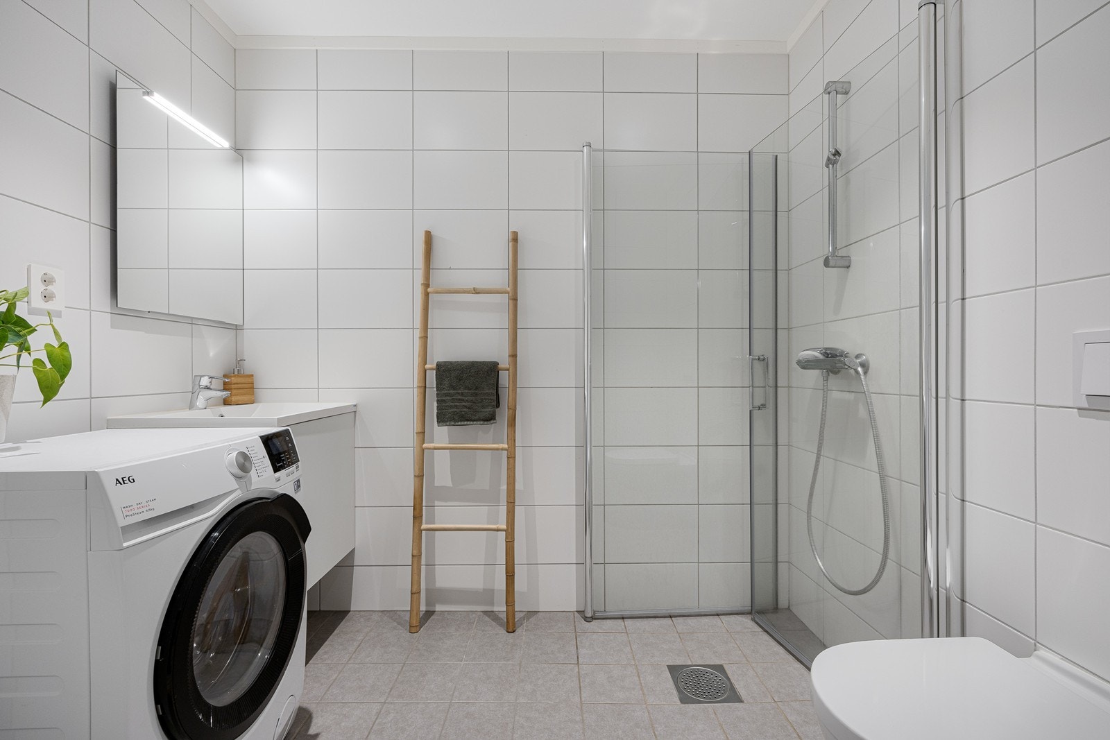 Badet i første etasje har vegghengt toalett, hvitt servantskap, speil med belysning, dusjhørne med innfellbare glassdører og opplegg for vaskemaskin Galleribilde