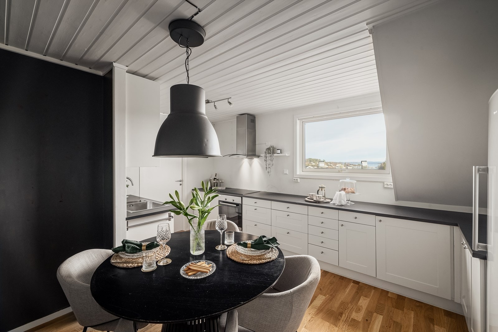 Kjøkkeninnredningen er i malt utførelse med en mørk, laminat benkeplate som står i fin kontrast til den lyse innredningen. Det er nedfelt benkebeslag og to kummer. Galleribilde