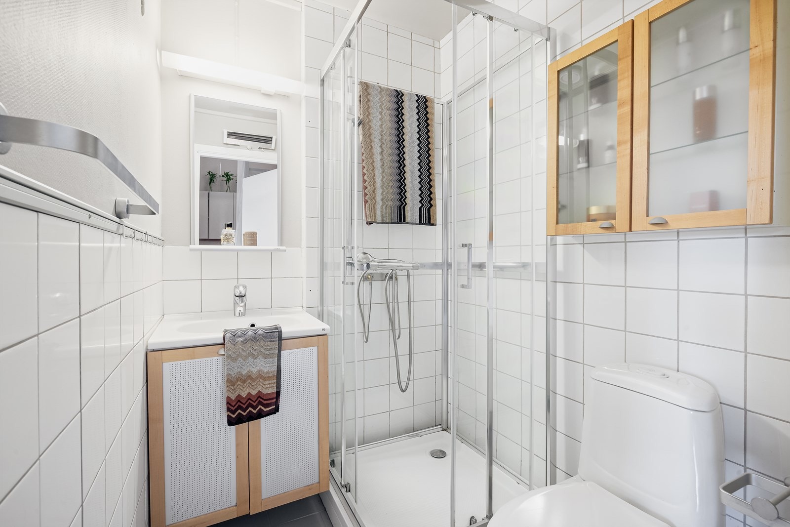 Baderommet i underetasjen inneholder gulvmontert toalett, innredning med servant og overhengt speil og et praktisk dusjkabinett. Galleribilde