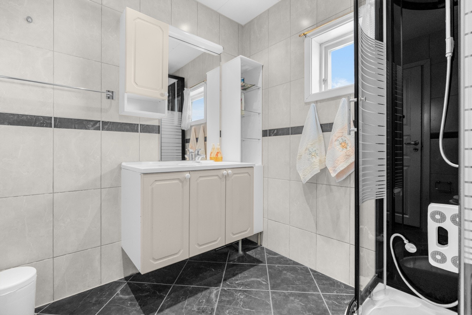 Lyst flislagt baderom som ble pusset opp i 2012. Baderomsinnredning med lyse profilerte fronter og heldekkende servant, speil med belysning og vegghengt skap over. Galleribilde