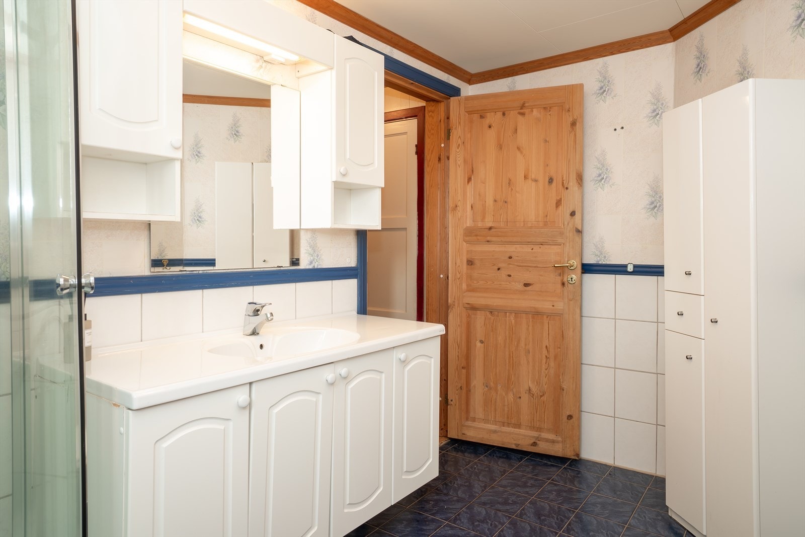 Badet er innredet med servant og skap, overskap med speil, dusjkabinett og gulvstående toalett. Galleribilde