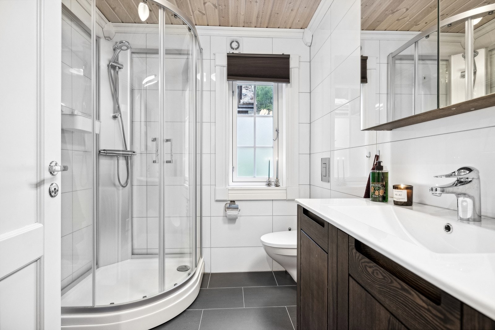 Badet i første etasje består av flislagt gulv og vegger, med ilagt varme i gulv. Her er det innredet med dusjkabinett, veggmontert toalett, Servant med underskap, og overskap med speil. Galleribilde