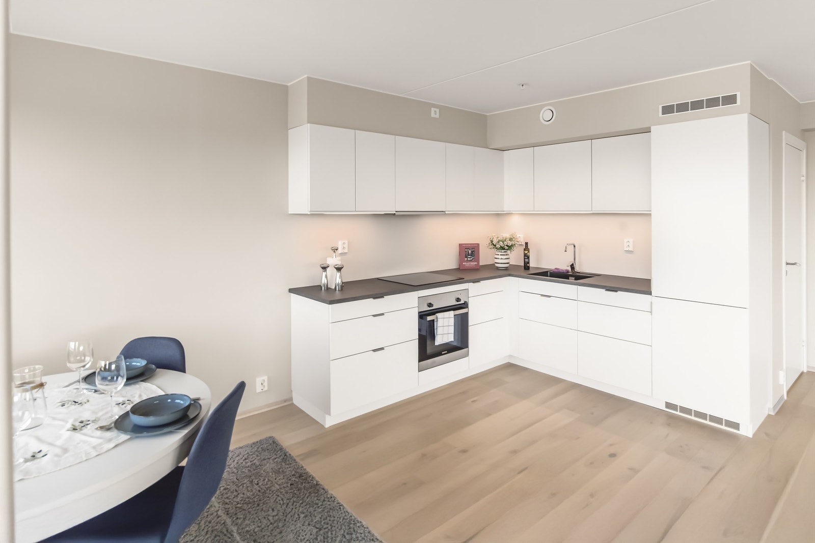 Et pent kjøkken med integrerte hvitevarer. Oppvaskmaskin, stekeovn, induksjonsplatetopp og kjøl/frys. Kjøkkenhette har vaskbart fettfilter, integrert belysning, LED-armatur og komfyrvakt Galleribilde