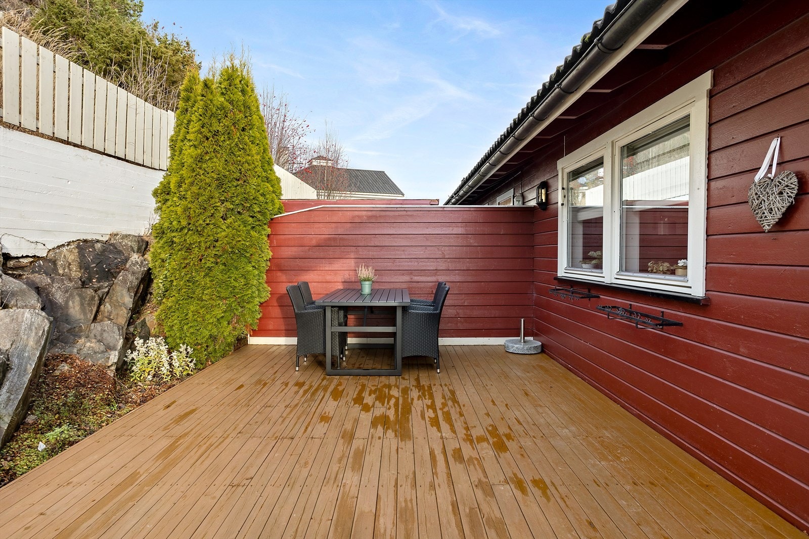 Ved inngangssiden er det en skjermet terrasse med beiset gulvdekke fra 2024. Terrassen strekker seg helt ut til fjellknausen og har noe beplantning i ytterkant. Galleribilde