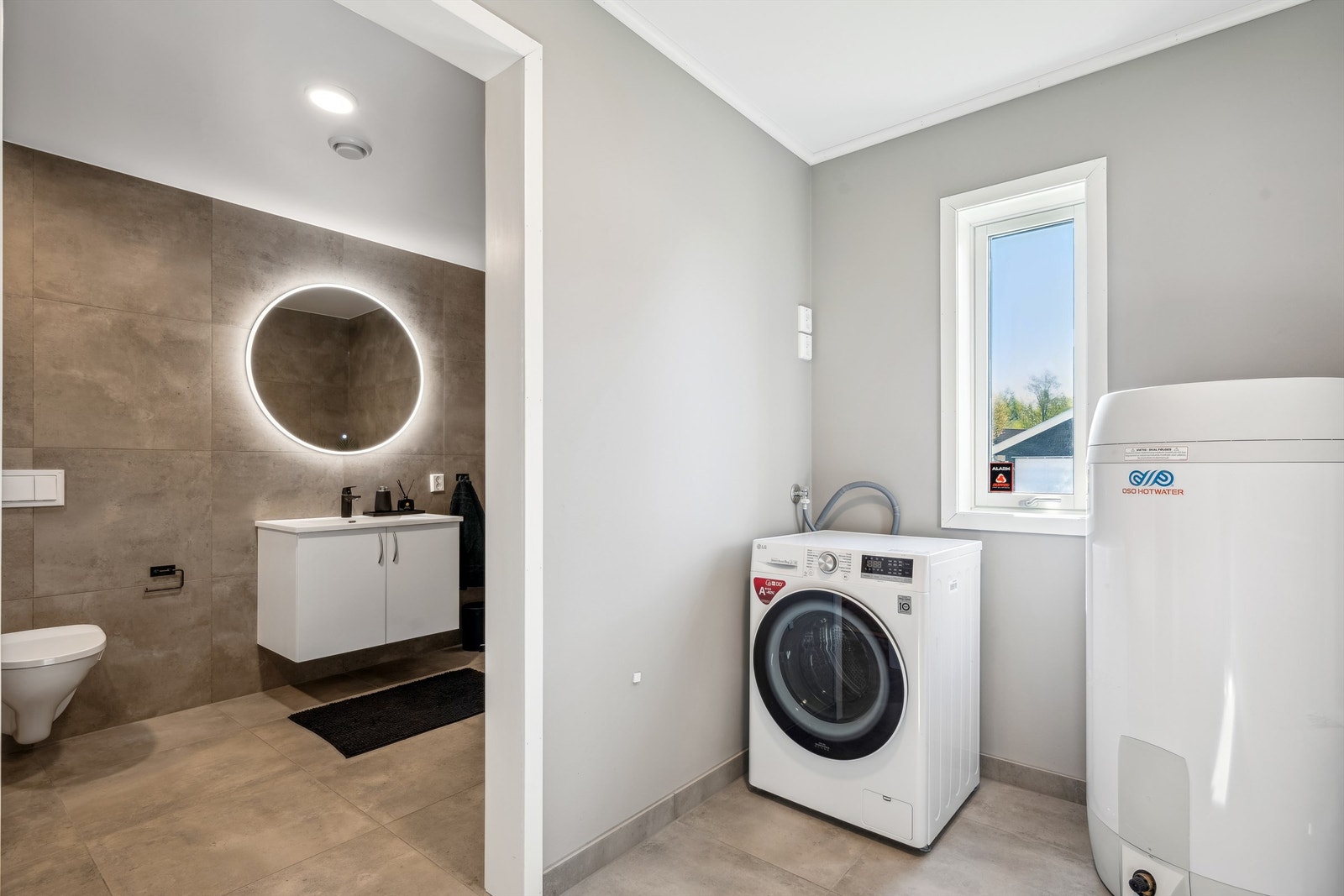 Det er åpen løsning til vaskerommet hvor man finner opplegg for vaskemaskin og boligens varmtvannsbereder Galleribilde