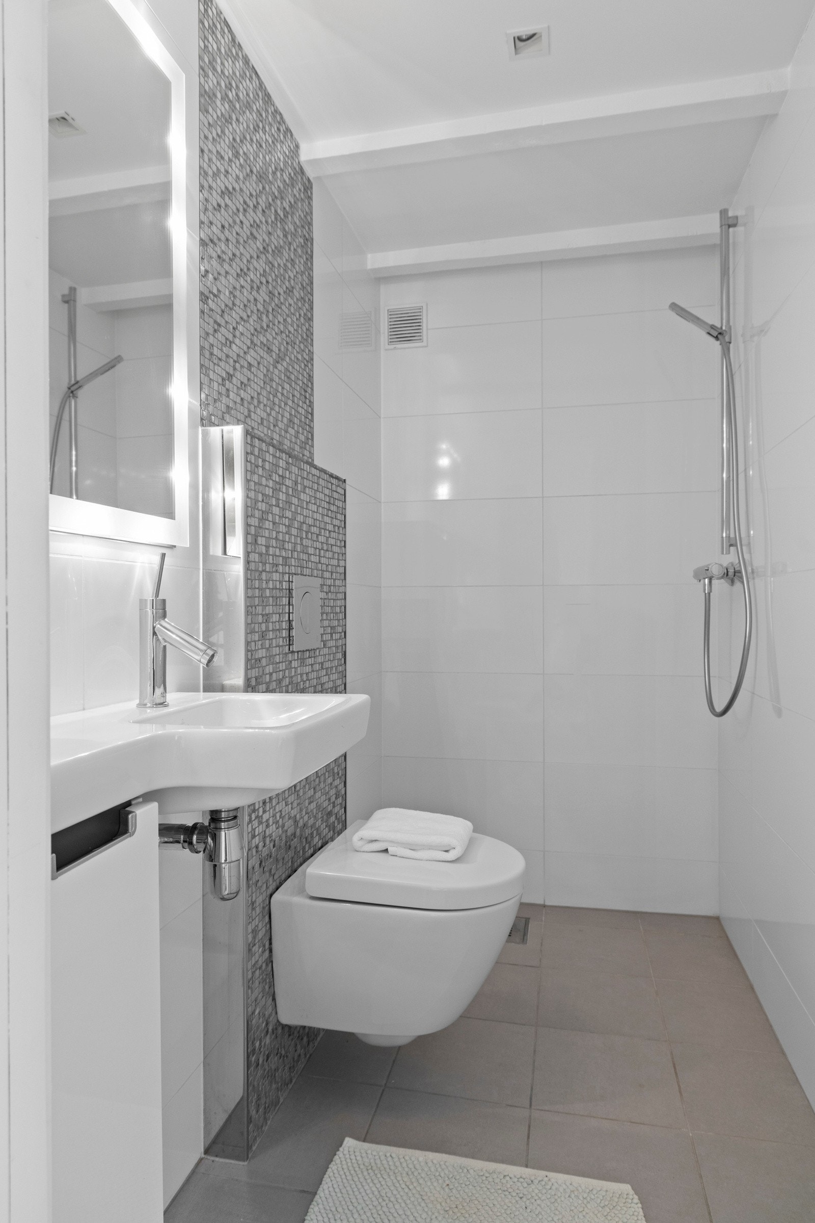 Baderom fra 2011. Det er flislagte veggflater og malt innvendig himling med synlige bjelker og downlights. Badet har flislagt gulv med vannbåren varme, vegghengt wc, servant og dusj i hjørne. Galleribilde