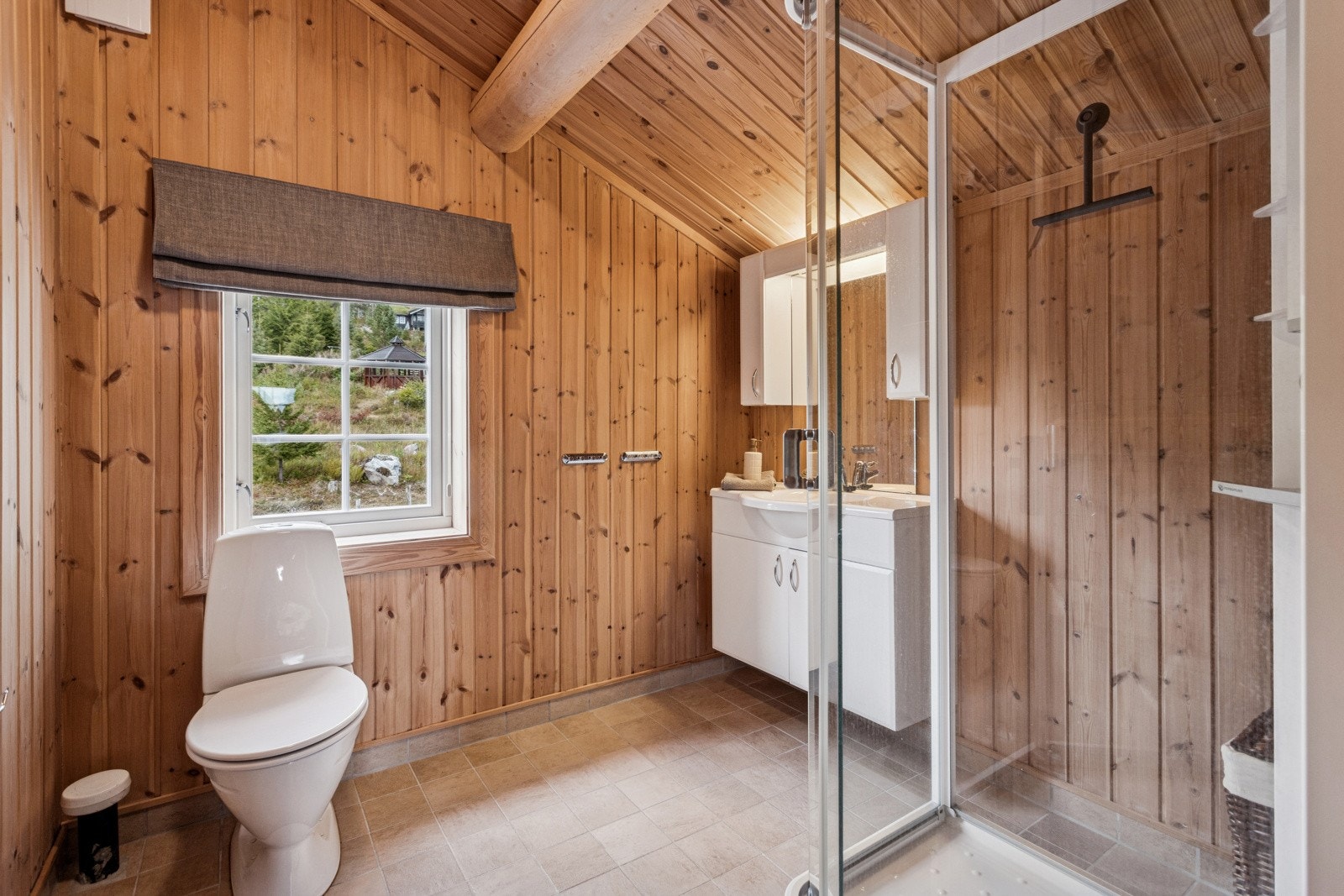 Baderom i 2. etasje med flislagt gulv og vegger med panel. Badet er utstyrt med toalett, dusjkabinett og baderomsinnredning med nedfelt servant og speil med belysning over. På badet er det åpen skråhimling og varmekabler i gulvet. Galleribilde