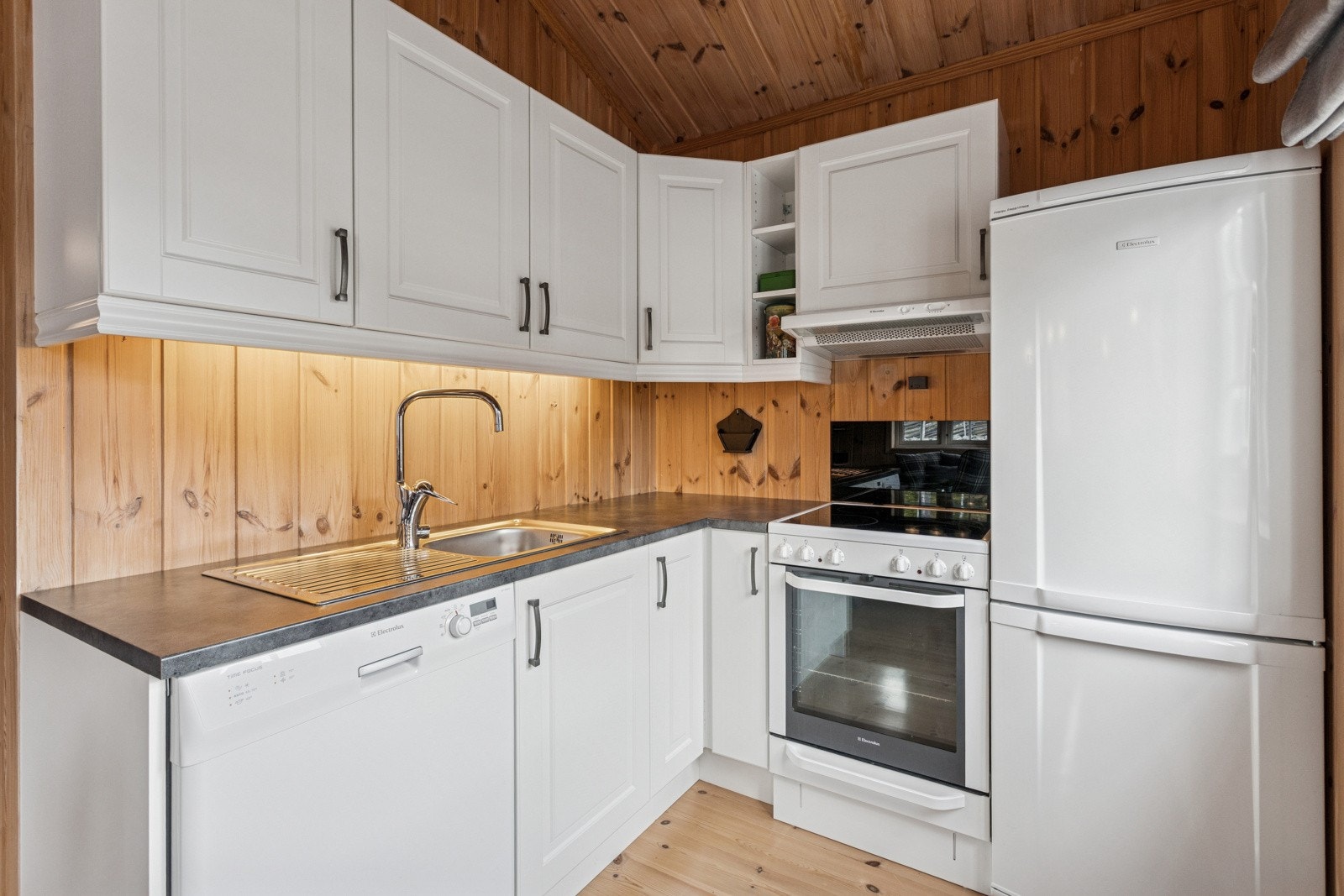 Kjøkken i åpen løsning fra stuen. Kjøkkeninnredning med lysmalte profilerte fronter og benkeplater i laminat. Opplegg for oppvaskmaskin og åpne løsninger for hvitevarer. Ventilator over komfyrplass. Galleribilde