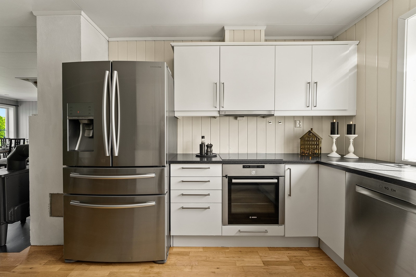 Vanntilkoblet kjøleskap med fryserskuffer og vanndispenser/isbitmaskin, oppvaskmaskin og induksjonstopp. Kjøkkenet har komfyrvakt. Galleribilde