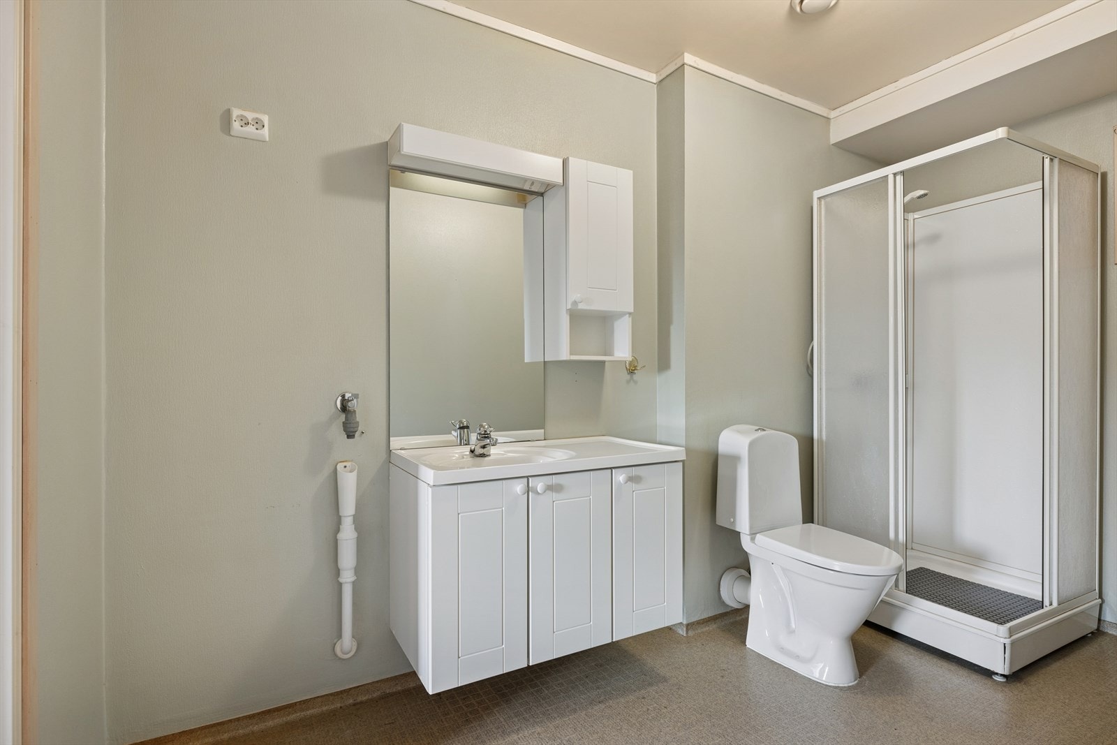 Baderommet er innredet med gulvmontert toalett, servant med skap og dusjkabinett. Galleribilde