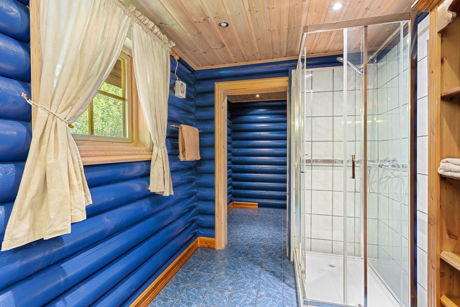 Badet i 1.etasje har flislagt gulv og god plass til oppbevaring. Veggene er utført i laft, malt i en varm blåfarge som gir rommet et særpreg. Galleribilde