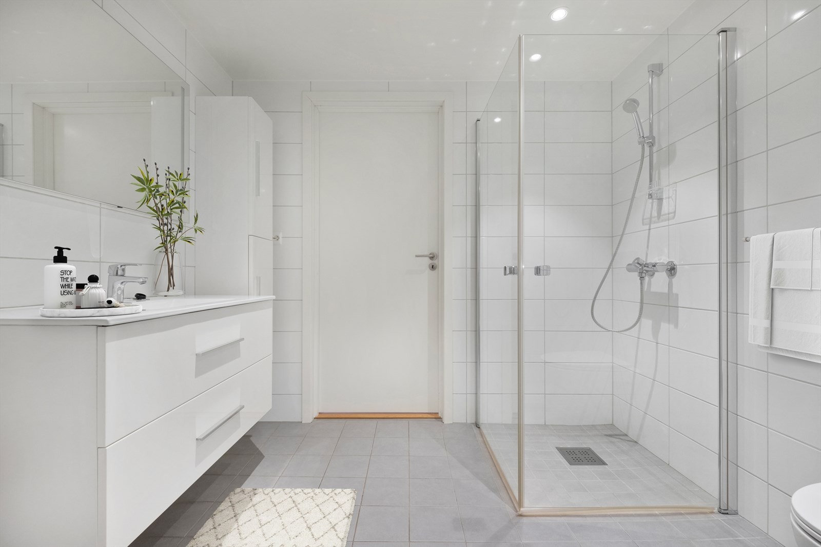 Pent bad som er utstyrt med vegghengt toalett, dusjdører og innredning med servant Galleribilde