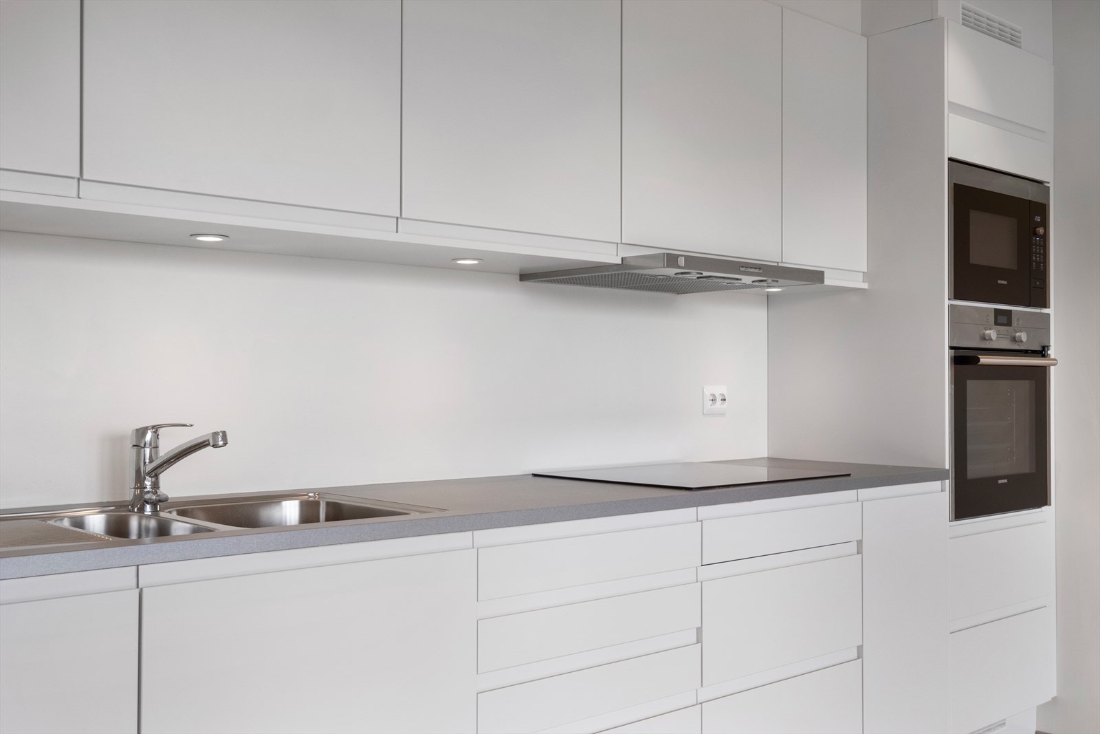 Kjøkkenet har innredning med hvite glatte fronter og benkeplate av laminat Galleribilde