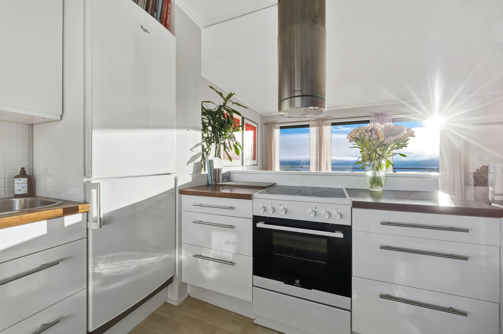 Elegant og lyst kjøkken med lys fra begge sider og nydelig utsikt inspirerer til gode matopplevelser Galleribilde