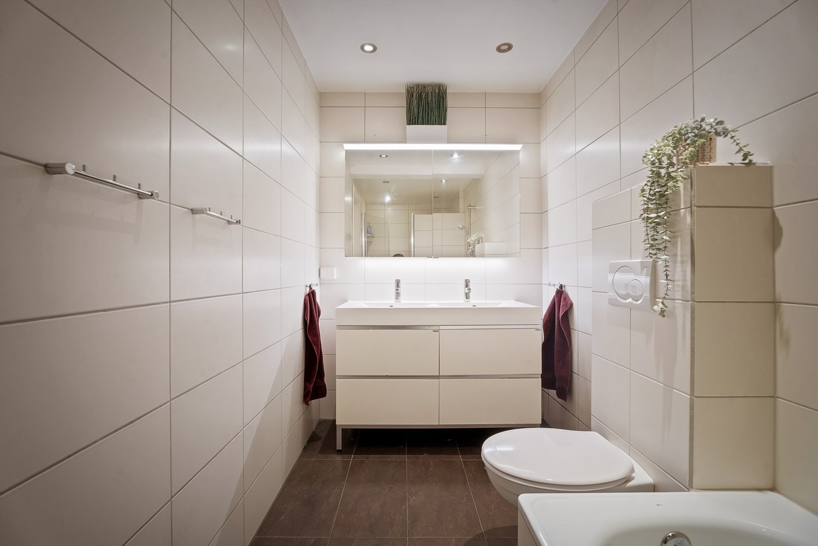 Romslig bad med heldekkende dobbel servant, innebygget badekar, dusjhjørne med svingbar glassdør og vegghengt toalett. Galleribilde