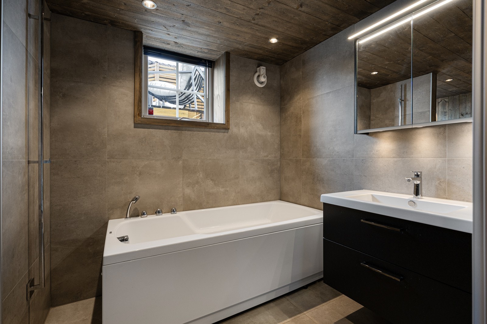 Innredning med heldekkende servant med mørke underskuffer. Over servanten er det speilskap med belysning Galleribilde