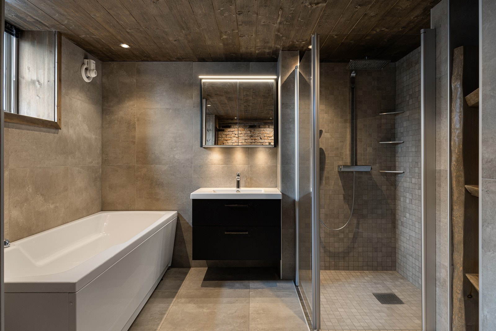 I det ene hjørnet er det et romslig dusjhjørne med regnfallsdusj, hånddusj og glassvegger. I det andre hjørnet er det badekar Galleribilde